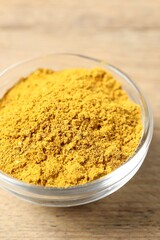 Curry powder in bowl on wooden table, closeup