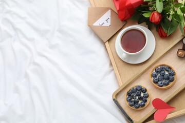 Tasty breakfast served in bed. Delicious tartlets, tea, flowers and card with phrase Love You on tray, top view. Space for text