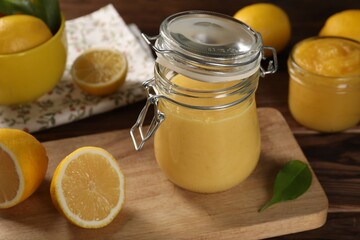 Delicious lemon curd in glass jars, fresh citrus fruits and green leaf on wooden table