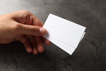 Man holding blank cards at black textured table, closeup. Mockup for design