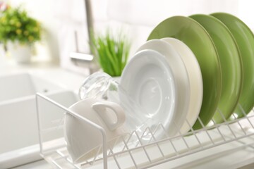 Drainer with different clean dishware, glass and cup indoors, closeup