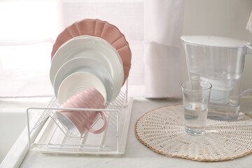 Drainer with different clean dishware, glass and cup on light table indoors