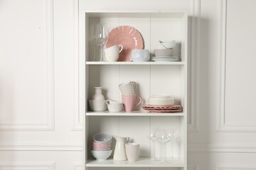 Different ceramic dishware and glasses on shelves in cabinet indoors