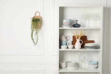 Different clean dishware and glasses on shelves in cabinet indoors