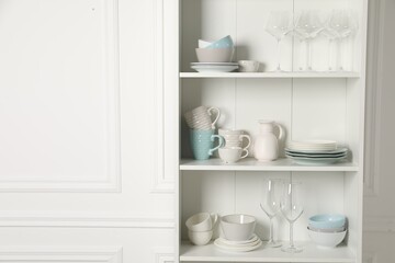 Different clean dishware and glasses on shelves in cabinet indoors