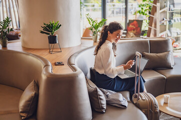 Businesswoman sitting in a hotel lobby, using laptop. Woman working on a business trip using online...