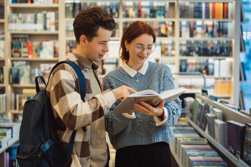 A young man and woman explore a selection of books in a cozy bookstore. They appear engaged and...