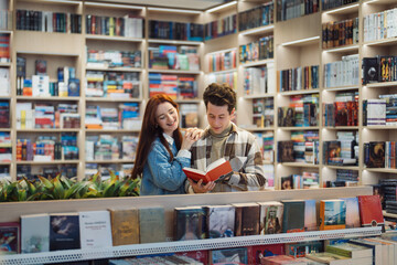 A joyful young couple shares a delightful moment while browsing through books in a well-organized...