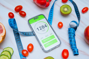 A calorie counting app displayed on a smartphone screen next to a tailor's measuring tape and a variety of healthy fruits and vegetables. Promoting mindful eating and nutrition tracking