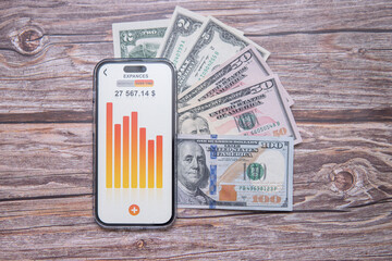 An app for household budgeting displayed on a smartphone screen next to American dollars. Concept illustrating income and expense planning. Rational approach to finances