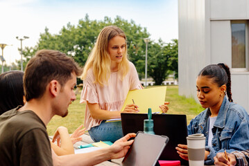 multiracial group of young students studying together or preparing a college project sitting on a bench on the university campus