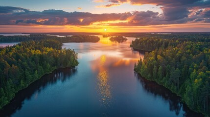 Breathtaking aerial perspective of the sun setting over a forest and lake, reflecting vibrant colors across the vast expanse
