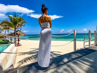 Young woman in sexy white swimwear contemplating the horizon of a paradisiacal Caribbean beach,...