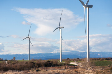 Three wind turbines are standing in a field with a cloudy sky in the background - obrazy, fototapety, plakaty