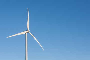 A wind turbine is standing tall in the sky, with a clear blue sky behind it
