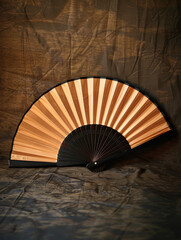 A traditional folding fan with black and gold hues, elegantly displayed against a dark background, highlighting its sophisticated and minimalistic design.