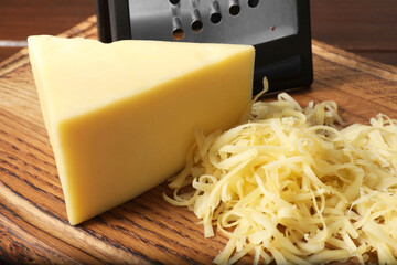 Grated and whole piece of cheese on wooden board, closeup