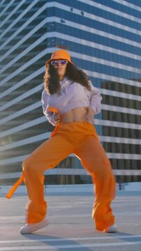 Vertical video. Sexy Twerk and freestyle clubber dancer practicing dance routine performing freestyle moves in city at golden sunset on city background 4K. African American young woman dancing