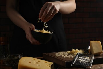 Woman with grated cheese at wooden table, closeup