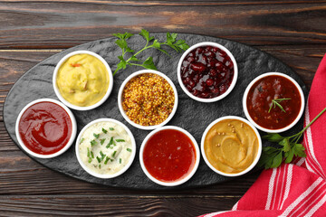 Different tasty sauces in bowls and parsley on wooden table, top view