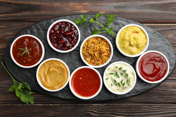 Different tasty sauces in bowls and parsley on wooden table, top view