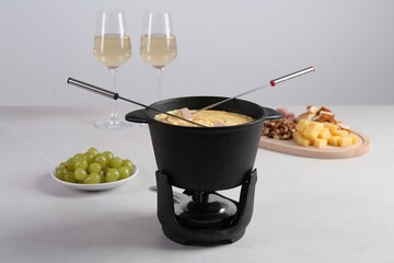 Fondue pot with tasty melted cheese, forks, wine and different snacks on white table
