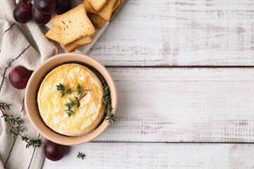 Tasty baked camembert in bowl, grapes, croutons and thyme on wooden table, flat lay. Space for text