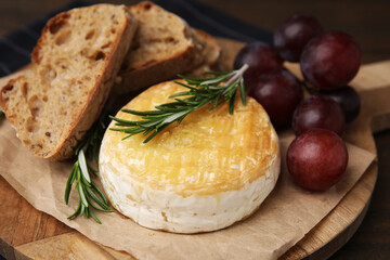 Tasty baked camembert, pieces of bread, grapes and rosemary on table, closeup