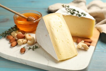 Tasty Camembert cheese with thyme, honey and nuts on light blue wooden table