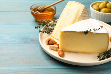 Tasty Camembert cheese with thyme and nuts on light blue wooden table, space for text