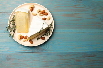 Tasty Camembert cheese with thyme and nuts on light blue wooden table, top view. Space for text