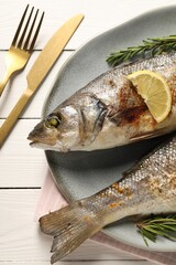 Delicious baked fish served on white wooden table, top view