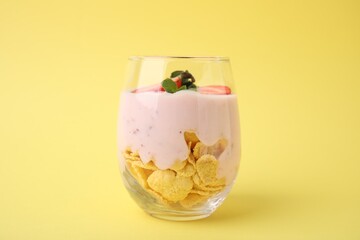 Glass with yogurt, strawberries and corn flakes on yellow background
