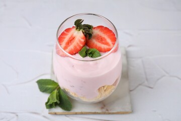 Glass with yogurt, strawberries and corn flakes on white textured table, closeup