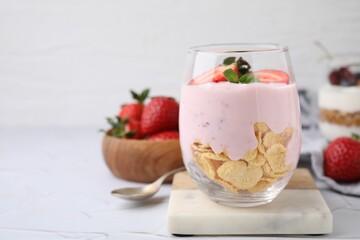 Glass with yogurt, strawberries and corn flakes on white textured table. Space for text
