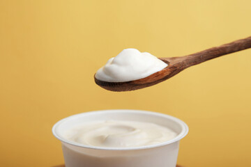 Eating delicious natural yogurt on yellow background