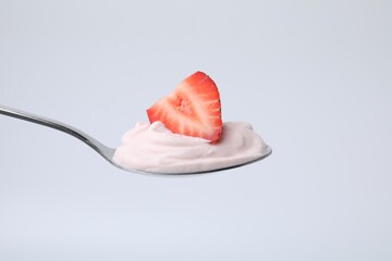 Delicious natural yogurt with fresh strawberry in spoon on light background