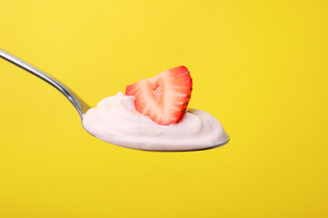 Delicious natural yogurt with fresh strawberry in spoon on yellow background