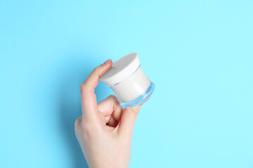 Woman holding jar of cream on light blue background, closeup