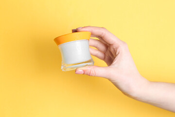 Woman holding jar of cream on yellow background, closeup