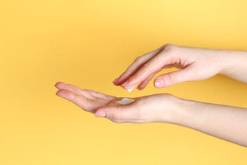 Woman applying cream on her hand against yellow background, closeup
