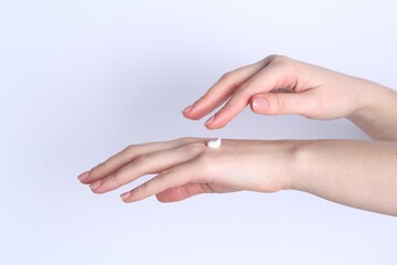 Woman applying cream on her hand against white background, closeup