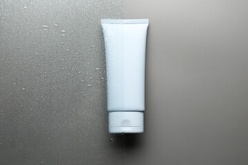 Tube with moisturizing cream on wet grey surface, top view