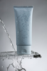 Moisturizing cream in tube on glass with water drops against grey background