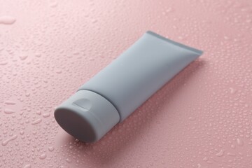 Moisturizing cream in tube on pink background with water drops, closeup