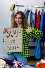 Young generation z girl holding banner with words swap not shop promoting sustainable fashion, conscious consumption, responsible consumerism. Concept of textile recycling, donation, fast fashion