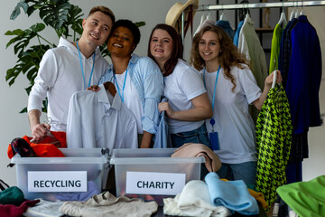 Group of volunteers, young women and man, sorting clothes in charitable foundation for charity...