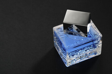 Blue men's perfume in bottle on black background, space for text