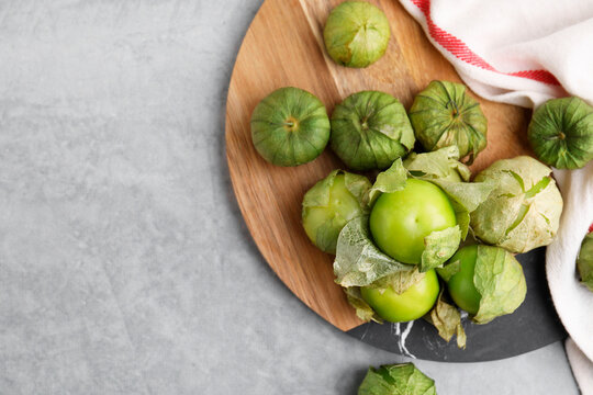 Fresh green tomatillos with husk on gray table, flat lay. Space for text