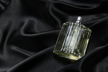 Luxury men's perfume in bottle on black satin fabric, above view. Space for text